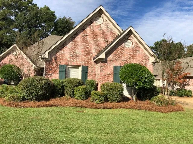 Brick home with clipped foundation shrubs, a crape myrtle and fresh pine straw, a Groundcare Landscape job
