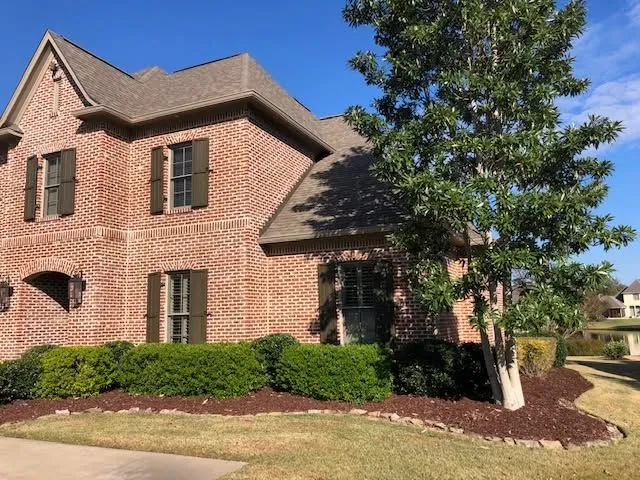 Tall brick home with a clipped hedge, a magnolia and a stone-edged mulch bed, a Groundcare Landscape job