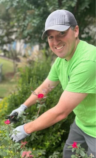 Groundcare Landscape crew member in a lime green shirt and gray cap pruning roses by hand