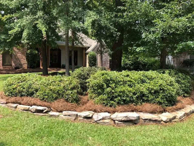 Stacked stone border holding a bed of shrubs and pine straw above the lawn, a Groundcare Landscape job