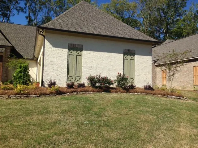 Painted brick home with roses in a stone-edged pine straw bed, a Groundcare Landscape job