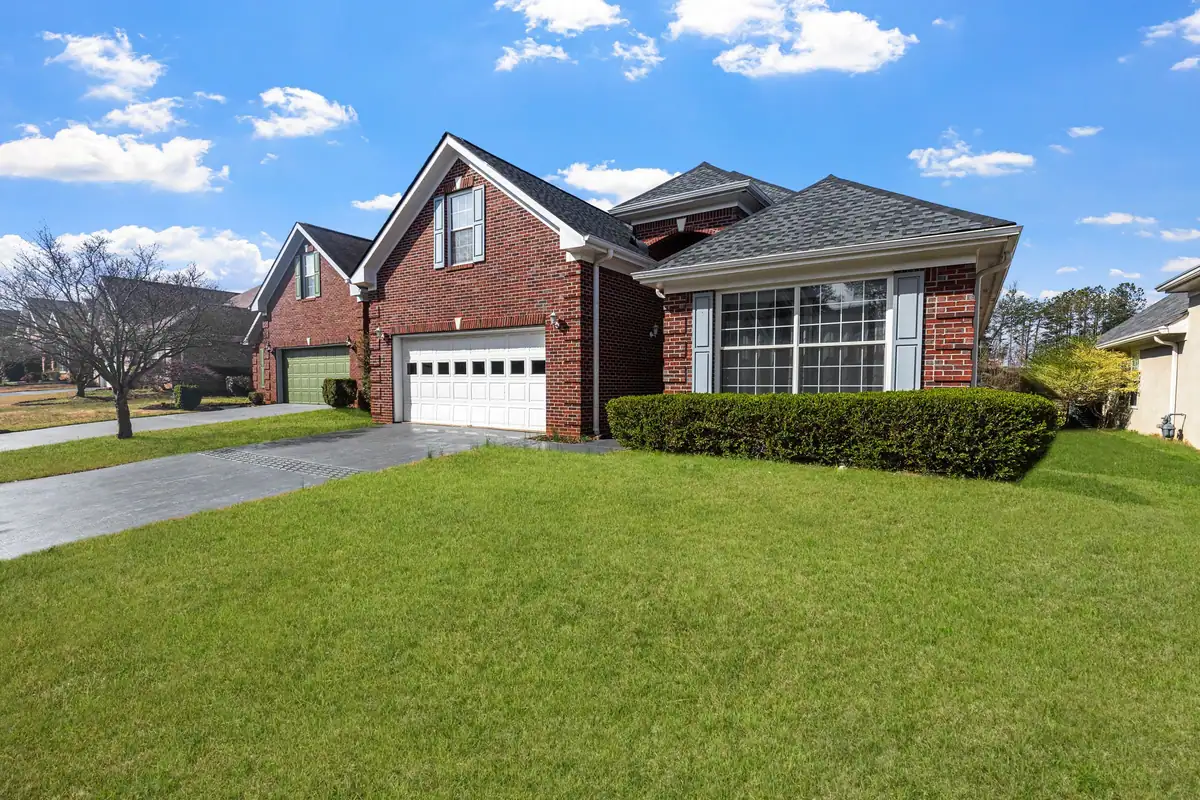 Brick home with a clipped hedge and a deep green front lawn under a blue sky