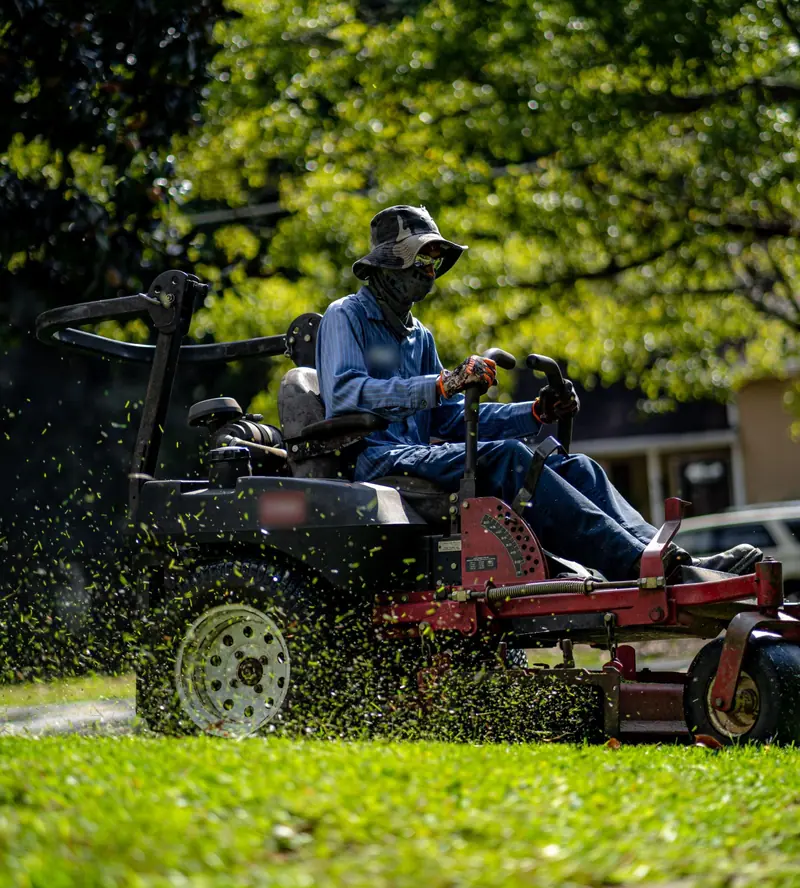 Crew member cutting a lawn on a zero-turn mower, clippings flying
